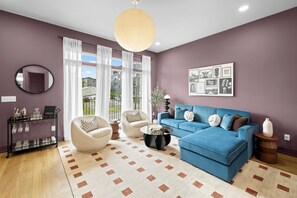 Ein Wohnzimmer mit einem blauen Sofa, weißen Sesseln, einem Couchtisch, einem runden Spiegel und einer Wand mit gerahmten Bildern.