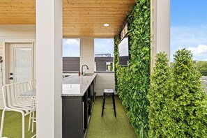 Eine moderne Küche mit Holzbalkendecke, einer Bar mit weißen Stühlen und einer grünen Wand mit Pflanzen.