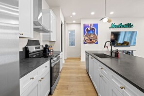 Eine moderne Küche mit weißen Schränken, einer schwarzen Arbeitsplatte und einer großen Kochinsel. An der Wand hängt ein Bild von einer Gitarre und ein Schild mit der Aufschrift 'Nashville' befindet sich über dem Fernseher.