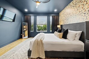 Ein Schlafzimmer mit einem Bett, einem Deckenventilator, einem Fernseher und einem Fenster mit Vorhängen.