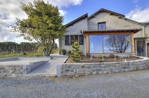 A modern house with a stone retaining wall, a wooden pergola, and a large window. - Charme des Bruyères - LANTIGNIE (LANTIGNIE)