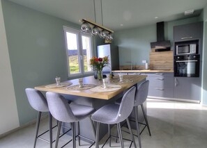 A modern kitchen with a dining table, bar stools, and a view of the outdoors. - Charme des Bruyères - LANTIGNIE (LANTIGNIE)