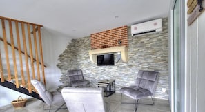 A modern living area with a stone wall, a flat-screen TV, and a wooden staircase. - Gîte du Mont Sombet - LES ARDILLATS (LES ARDILLATS)