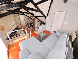 Ein Loft-Zimmer mit freiliegenden Balken, einer Treppe, einem grauen Sofa und einem kleinen Tisch.