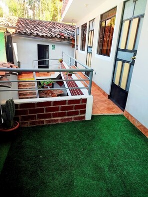 A courtyard with a brick wall, artificial grass, a cactus, and a small building with a tiled roof.