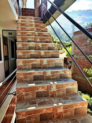 Un escalier en pierre menant à un balcon, une plaque portant le numéro « 205 », et une vue sur un paysage vallonné.