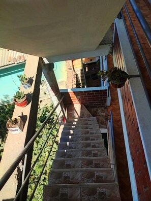 Un escalier orné de plantes en pot de chaque cÎté, un mur de briques et une rambarde en métal.