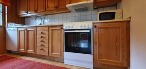 Eine Küche mit Holzausstattung, einem weißen Herd, einer Mikrowelle und einem roten Teppich.