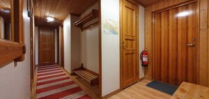 Ein Holzbodenkorridor mit einem rot-weiß gestreiften Teppich, einer hölzernen Bank und einem an der Wand befestigten Feuerlöscher.