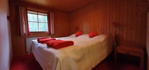 Ein Zimmer mit Holzwänden, einem großen Bett, einem Fenster mit Vorhängen und einer Bank.