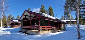 Eine Holzhütte mit einer Veranda, umgeben von Schnee und Bäumen.