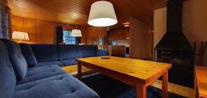 Ein gemütliches Blockhaus-Interieur mit Holzbalkendecke, einer Couch, einem Tisch und einem Kamin.