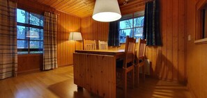 Ein Holzblock-Interieur mit einem Esstisch, Stühlen, einer Pendelleuchte und großen Fenstern.