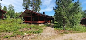 Eine Holzhütte mit Veranda, umgeben von Bäumen und einem Kiesweg.