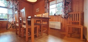 Ein Holzinterieur mit einem Esstisch und Stühlen, einem Heizkörper und floralen Vorhängen.