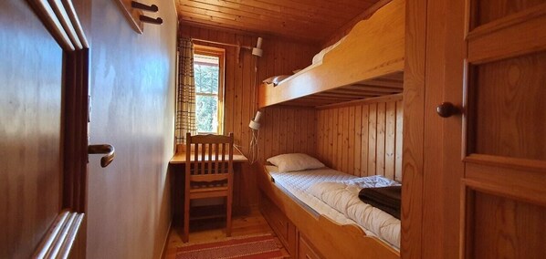 Ein kleines Zimmer mit Etagenbetten, einem Holztisch und einem Stuhl.