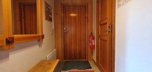 Eine Holztür mit an der Wand befestigtem Feuerlöscher, ein kleiner Tisch und eine Fußmatte im Eingangsbereich.