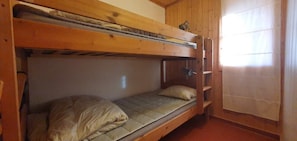Ein Schlafzimmer mit Etagenbetten, Holzboden und einem Fenster mit Vorhängen, inklusive einer Leitern.