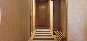 Ein schmaler Korridor mit einer Holztür am Ende, Teppichboden und Holzvertäfelung an den Wänden.