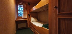 Ein kleines, holzgetäfeltes Zimmer im Blockhausstil mit einem Etagenbett, einem Fenster mit Vorhang und einer Heizung.