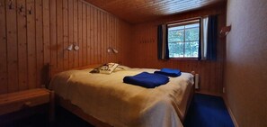 A wooden-paneled room with a bed, a window with curtains, and a bench.