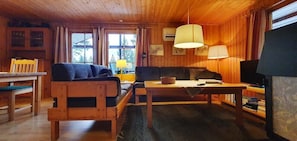 Ein Interieur einer Holzhütte mit einer Couch, einem Tisch, einem Fernseher und einem Fenster.