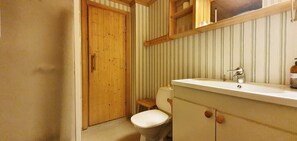 A bathroom with a wooden door, a toilet, a sink with a mirror, and striped wallpaper.