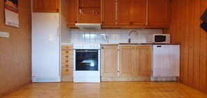 Eine Küche mit Holzausstattung, einem weißen Kühlschrank, einer Mikrowelle, einem Backofen und einem Spülbecken.