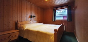 Ein Zimmer mit Holzwandverkleidung, einem Bett, einem Nachttisch und einem Fenster mit Vorhängen.