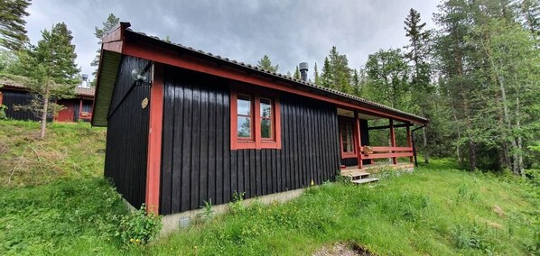 A black wooden cabin with red trim, a porch, and a small deck.
