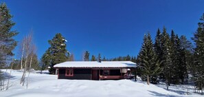 A cabin with a snow-covered roof, surrounded by trees and a clear sky.