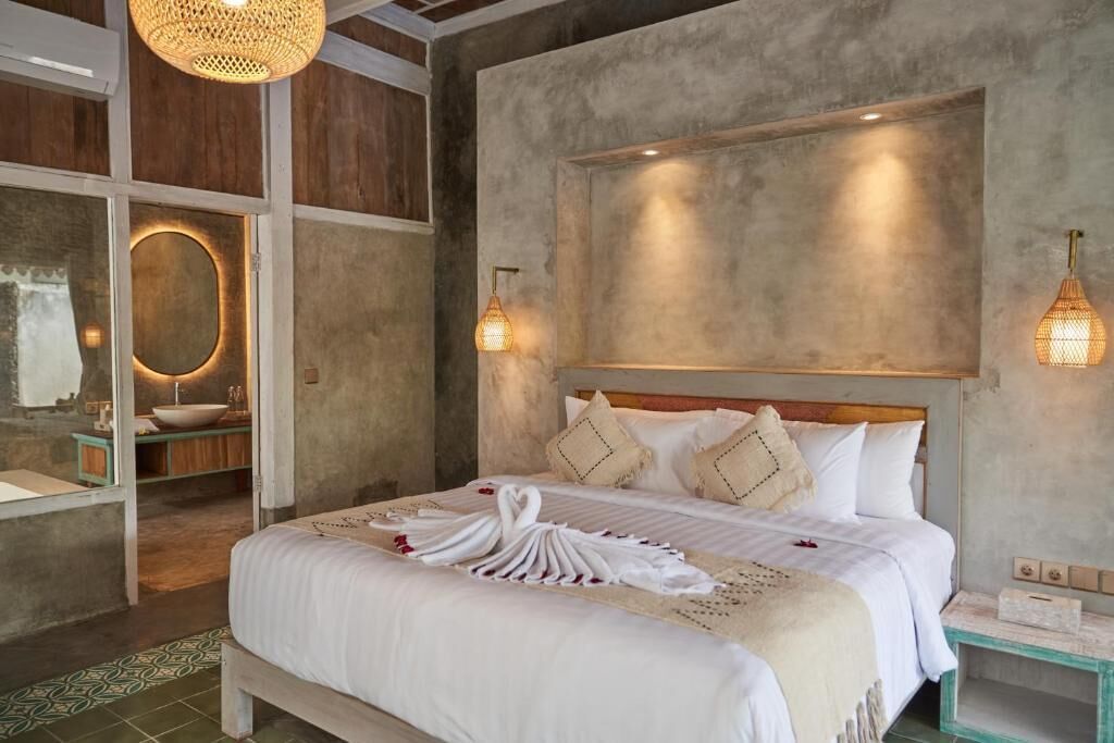 Ein Schlafzimmer mit einem Bett, Nachttischen, einer Wandleuchte und einem Badezimmer mit Waschbecken und Spiegel.