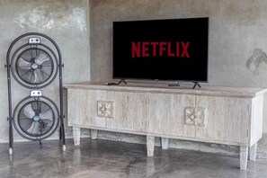 Ein Fernseher mit dem Netflix-Logo, ein Holzkabinett mit Zierleisten und ein Standventilator.