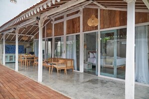 Ein überdachter Außenbereich mit Holzterrasse, einem Esstisch mit Stühlen und einem gläsernen Raum mit einem Bett.