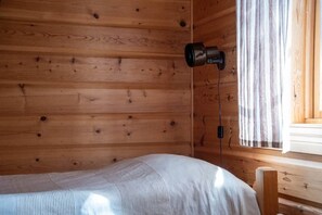 Ein Zimmer in einer Holzhütte mit einem Bett, einem Fenster mit Vorhängen und einer angebrachten Kamera.
