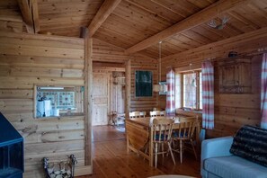 Interior de una cabaña de madera con comedor, cocina y una acogedora sala de estar.