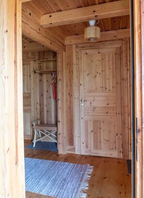 Un intérieur en bois avec une porte, un luminaire suspendu et une petite table accompagnée d’une chaise.