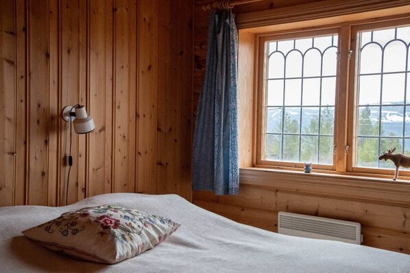 Une chambre dans un chalet en bois, avec un lit, une fenêtre donnant sur un paysage agréable et une lampe fixée au mur.