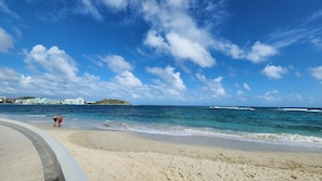A beach with a clear sky, a sandy shore, and a few people walking.