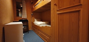 Ein kleines Zimmer mit Etagenbett, Schreibtisch, Stuhl und Kühlschrank.
