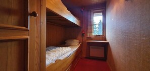 Una habitación pequeña con una cama litera, una mesita y una ventana que da a los árboles.
