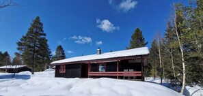 Eine Hütte mit schneebedecktem Dach, umgeben von Bäumen, und einem strahlend blauen Himmel.