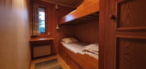 Ein kleines Zimmer mit Holzwänden, einem Stockbett, einem Schreibtisch und einem Fenster mit Vorhängen.