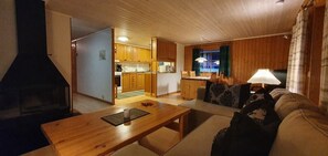 Ein gemütliches Wohnzimmer mit Kamin, Holzmöbeln und einer Küche im Hintergrund.