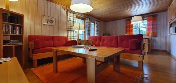 Ein gemütlicher Raum mit Holzbalkendecke, einem roten Sofa, einem Holztisch und einem Bücherregal.