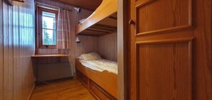 Ein kleines Zimmer mit Etagenbett, einem schmales Fenster mit Vorhängen und einer Heizung.