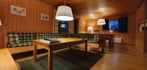 A cozy cabin interior with a wooden floor, a wooden table, a green and white checkered sofa, and a dining table with chairs. - Sauna | Wi-Fi | Terrace | Wood stove | Cable TV (Lofsdalen)