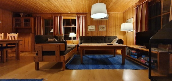 Ein Holzinnenraum mit einer Couch, einem Tisch, Stühlen, einem Fernseher und einem Kamin.