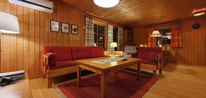 Ein Zimmer mit Holzwänden, einem roten Sofa, einem Holztisch und einer Lampe.