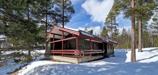 Eine Holzhütte mit rotem Dach und grünen Wänden, umgeben von Schnee und Bäumen.